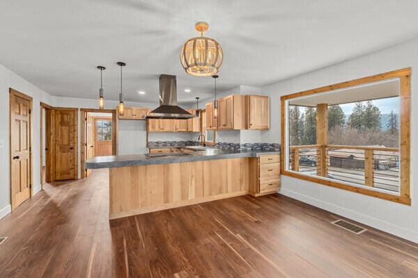 kitchen with island range hood, dark hardwood / wood-style flooring, decorative light fixtures, kitchen peninsula, and light brown cabinets