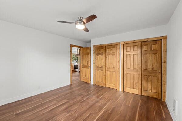 unfurnished bedroom with dark wood-type flooring, two closets, and ceiling fan