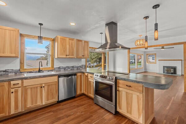 kitchen featuring appliances with stainless steel finishes, pendant lighting, sink, island exhaust hood, and kitchen peninsula