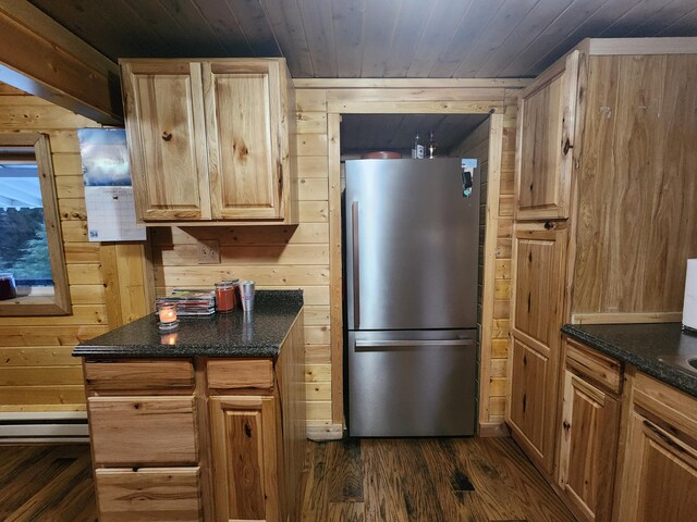 kitchen with dark stone countertops, wooden walls, wooden ceiling, and stainless steel fridge