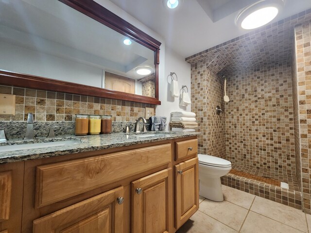 bathroom featuring toilet, tasteful backsplash, a tile shower, tile patterned flooring, and vanity