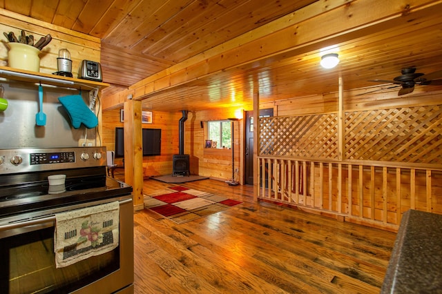 kitchen featuring hardwood / wood-style floors, wooden ceiling, stainless steel electric range oven, a wood stove, and wood walls