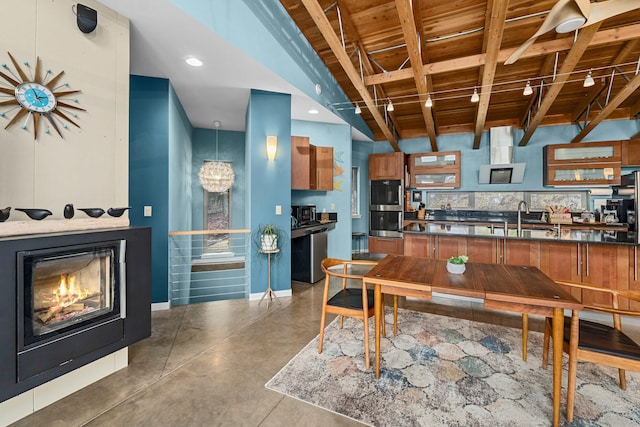 dining space featuring a glass covered fireplace, finished concrete floors, recessed lighting, beamed ceiling, and wooden ceiling