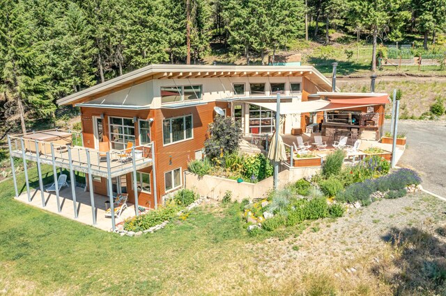 back of house with a lawn, a view of trees, a patio area, and a deck