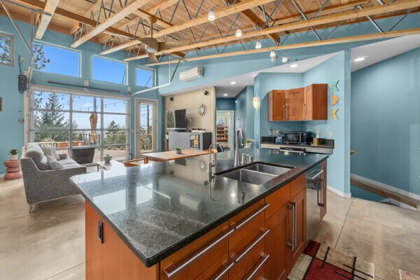 kitchen with a sink, open floor plan, finished concrete floors, a high ceiling, and an island with sink