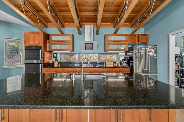 kitchen featuring a sink, brown cabinetry, a spacious island, double wall oven, and freestanding refrigerator