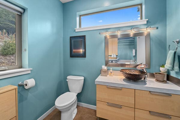 half bath with baseboards, toilet, and vanity