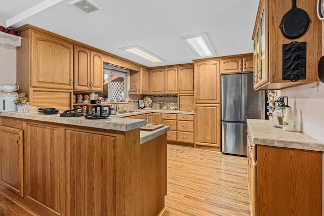 kitchen featuring sink, backsplash, stainless steel refrigerator, kitchen peninsula, and light wood-type flooring