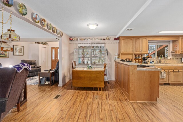 kitchen with sink, a textured ceiling, light wood-type flooring, and a kitchen island