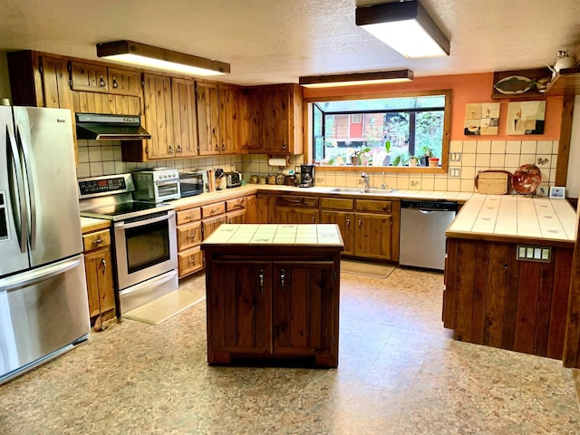 59 Bisbee Creek Ln, Kettle Falls, WA 99141 - kitchen with appliances with stainless steel finishes, tile countertops, under cabinet range hood, tasteful backsplash, and a center island