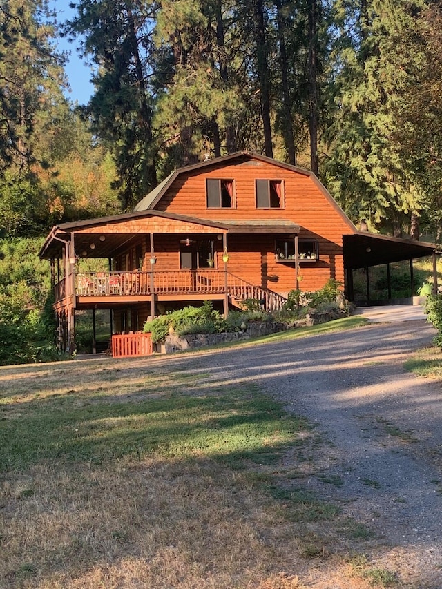 59 Bisbee Creek Ln, Kettle Falls, WA 99141 - view of front facade featuring a gambrel roof, gravel driveway, an attached carport, a wooden deck, and a front yard