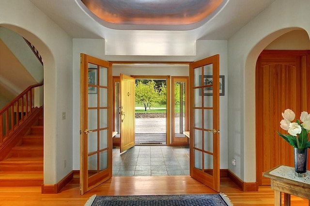 foyer with french doors, arched walkways, wood finished floors, baseboards, and stairs