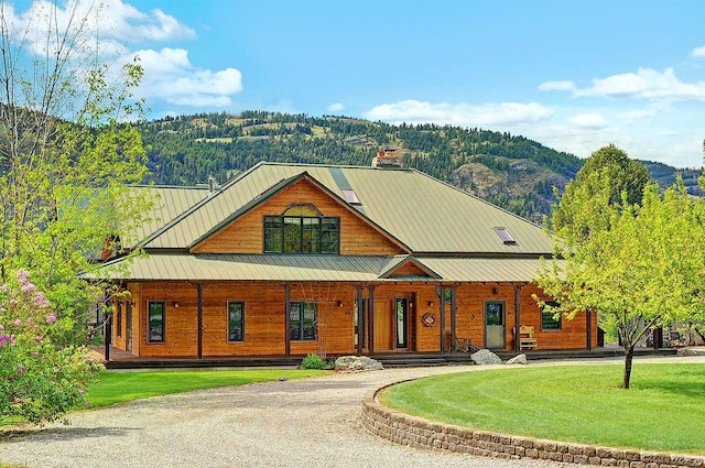 view of front of home featuring a front lawn, covered porch, curved driveway, a chimney, and a standing seam roof