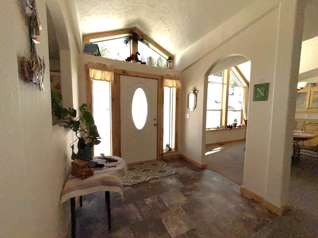 foyer entrance featuring arched walkways, vaulted ceiling, a textured ceiling, and baseboards