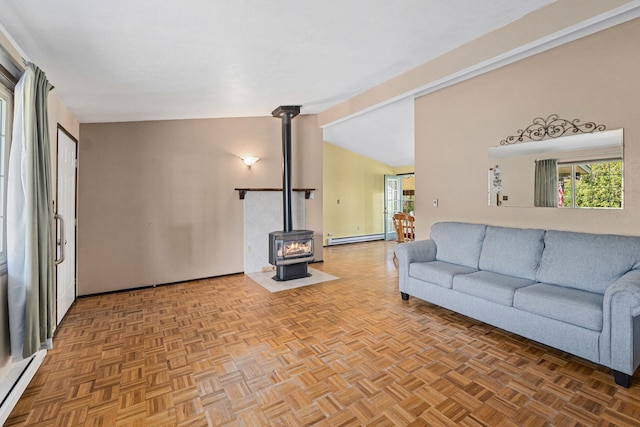 living room featuring a wood stove, a baseboard heating unit, healthy amount of natural light, a baseboard radiator, and vaulted ceiling