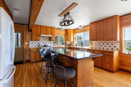 3439 Northport Flat Creek Rd Unit B, Kettle Falls, WA 99141 - kitchen with freestanding refrigerator, under cabinet range hood, brown cabinets, light wood-style floors, and decorative backsplash
