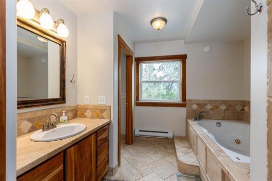 3439 Northport Flat Creek Rd Unit B, Kettle Falls, WA 99141 - bathroom with a baseboard radiator, vanity, a jetted tub, and decorative backsplash