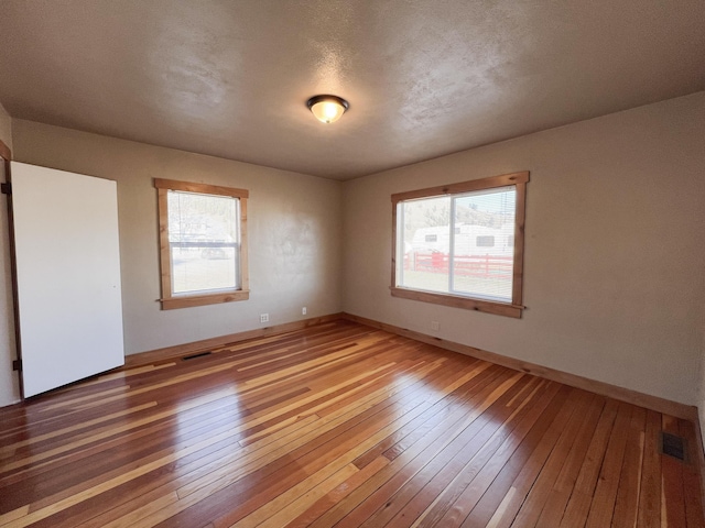 unfurnished room featuring a wealth of natural light, hardwood / wood-style floors, and a textured ceiling