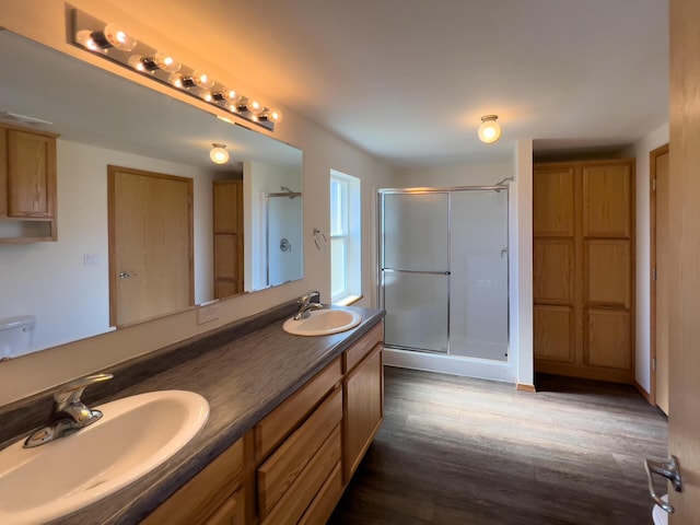 bathroom with a stall shower, double vanity, a sink, and wood finished floors