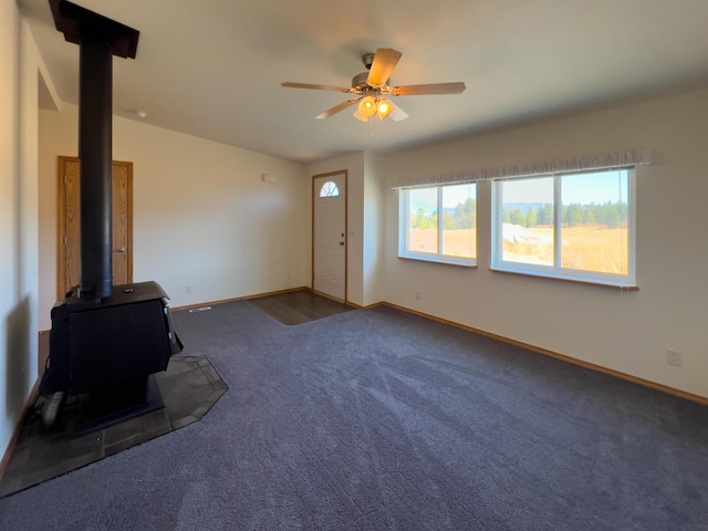 unfurnished living room with a wood stove, a ceiling fan, baseboards, and carpet flooring