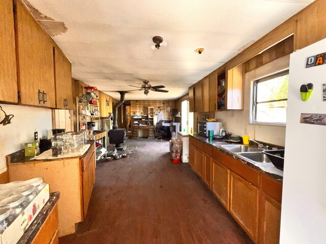 kitchen with white fridge, sink, a wood stove, dark colored carpet, and ceiling fan