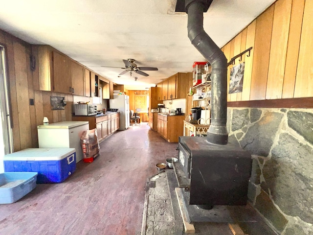 kitchen with white refrigerator, a wood stove, wood walls, ceiling fan, and fridge