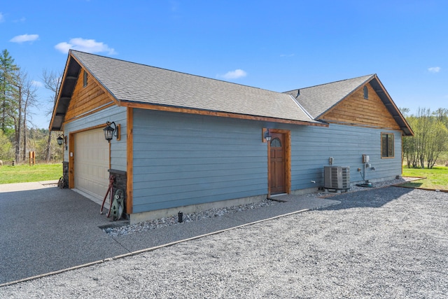 view of side of home with central AC, roof with shingles, and a garage