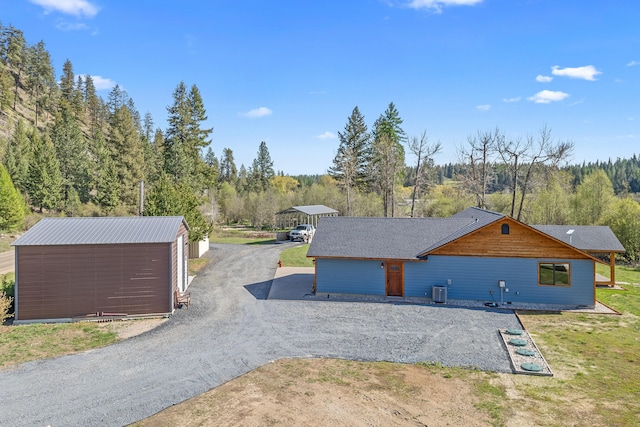 exterior space with dirt driveway, an outdoor structure, and a wooded view