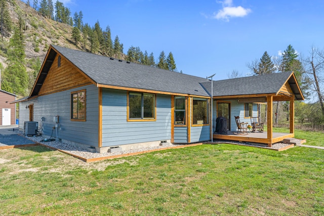 rear view of house featuring central AC unit, a yard, a deck, and a shingled roof