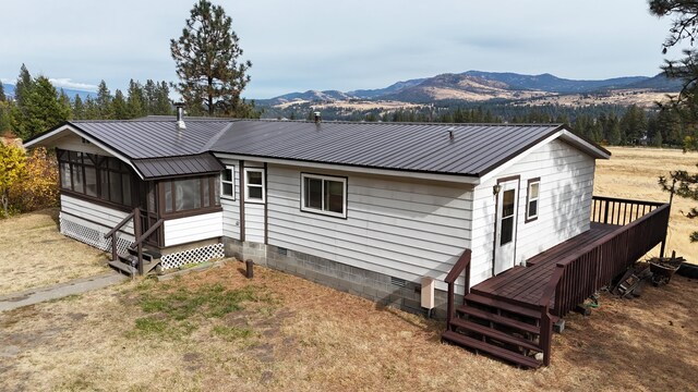 back of property featuring a deck with mountain view, a sunroom, and metal roof