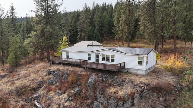 back of house featuring metal roof, a view of trees, and a deck