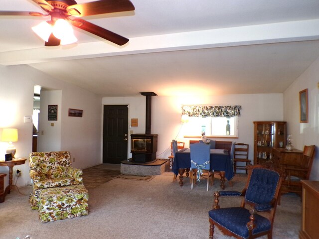 carpeted living room with lofted ceiling with beams, ceiling fan, and a wood stove