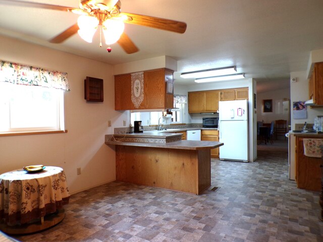 kitchen with a ceiling fan, a sink, white appliances, a peninsula, and brown cabinetry