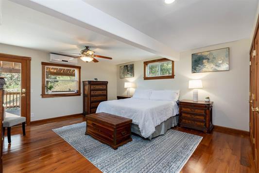 bedroom with baseboards, wood finished floors, an AC wall unit, and beamed ceiling