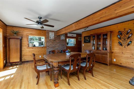 dining room with wooden walls, a ceiling fan, beamed ceiling, light wood-type flooring, and a wall mounted AC