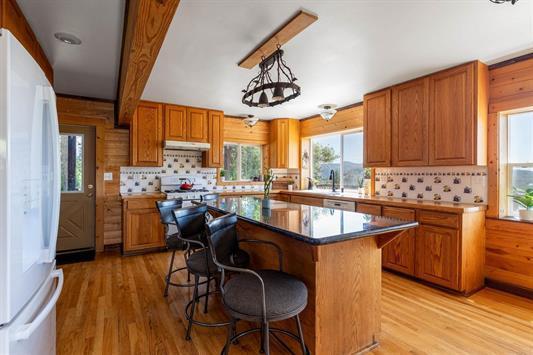 kitchen featuring a breakfast bar area, brown cabinetry, freestanding refrigerator, light wood-style floors, and under cabinet range hood