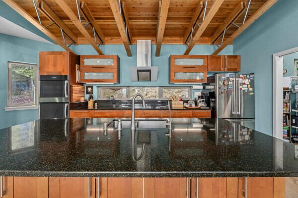 kitchen featuring high end refrigerator, brown cabinetry, a large island, double oven, and a sink