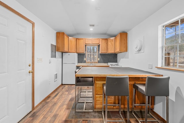 kitchen featuring dark wood-type flooring, a kitchen breakfast bar, white refrigerator, decorative backsplash, and vaulted ceiling