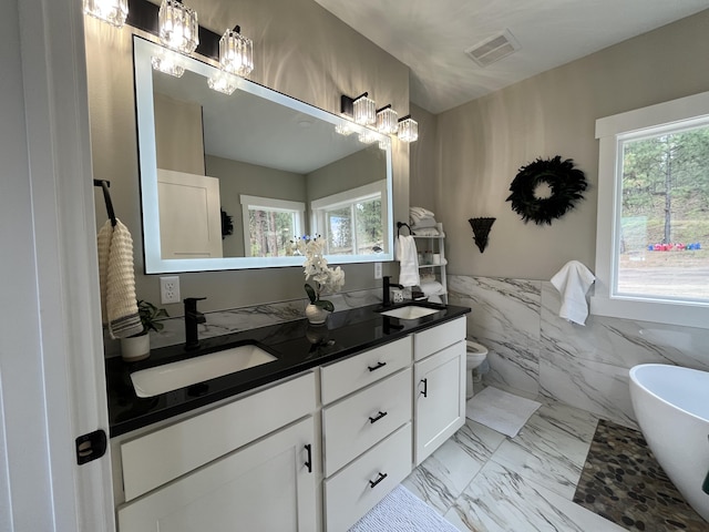full bath featuring a chandelier, healthy amount of natural light, marble finish flooring, a freestanding bath, and wainscoting