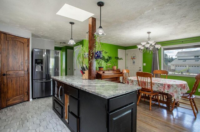 kitchen featuring a textured ceiling, a kitchen island, black microwave, hanging light fixtures, and stainless steel fridge