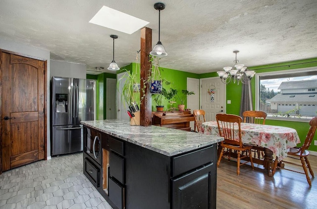 1001 E Hawthorne Ave, Colville, WA 99114 - kitchen featuring a textured ceiling, a kitchen island, black microwave, hanging light fixtures, and stainless steel fridge