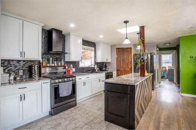 kitchen with wall chimney range hood, a kitchen island, white cabinetry, and stainless steel gas stove