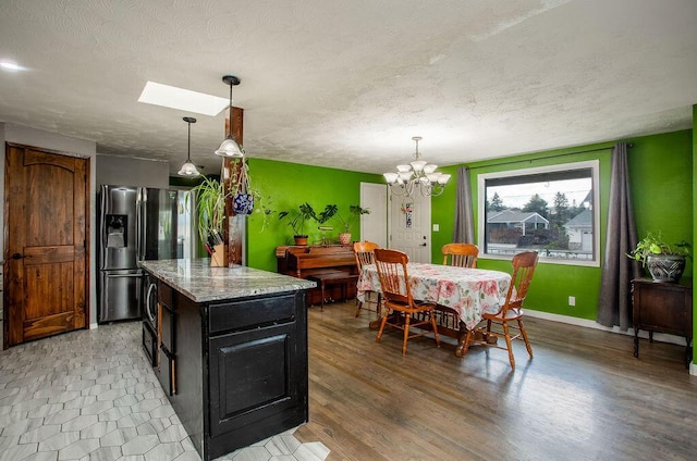 kitchen featuring stainless steel refrigerator with ice dispenser, hanging light fixtures, light stone counters, a textured ceiling, and a skylight