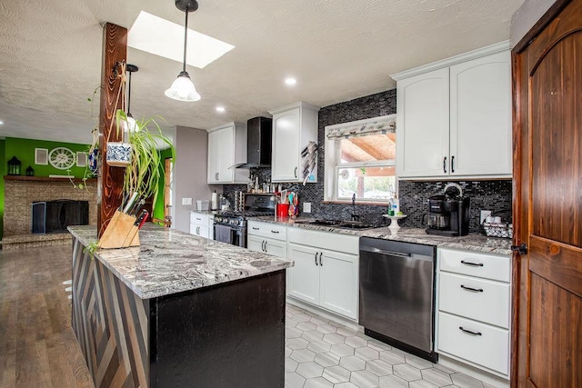 kitchen with wall chimney exhaust hood, sink, decorative light fixtures, white cabinetry, and stainless steel appliances