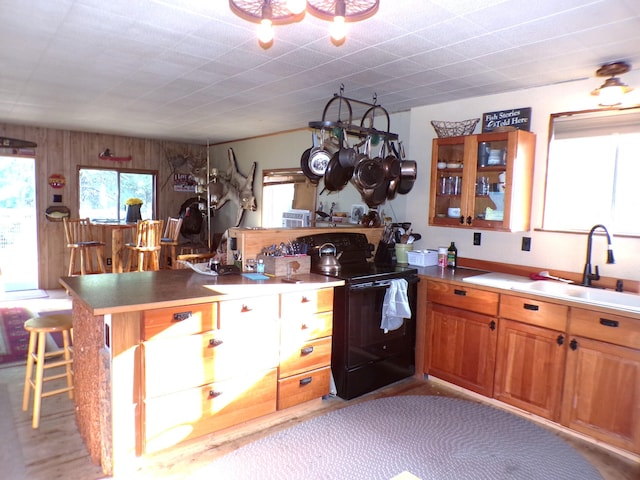 kitchen featuring brown cabinets, a breakfast bar, a sink, black electric range, and a peninsula