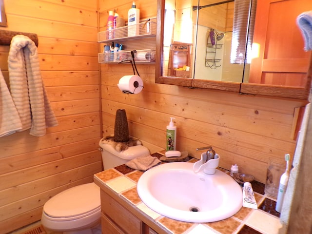 bathroom featuring wood walls, toilet, and vanity