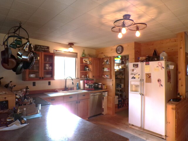 kitchen with a sink, open shelves, white refrigerator with ice dispenser, wood walls, and dishwasher