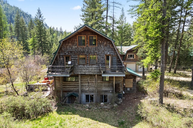 rear view of property with a gambrel roof and a forest view