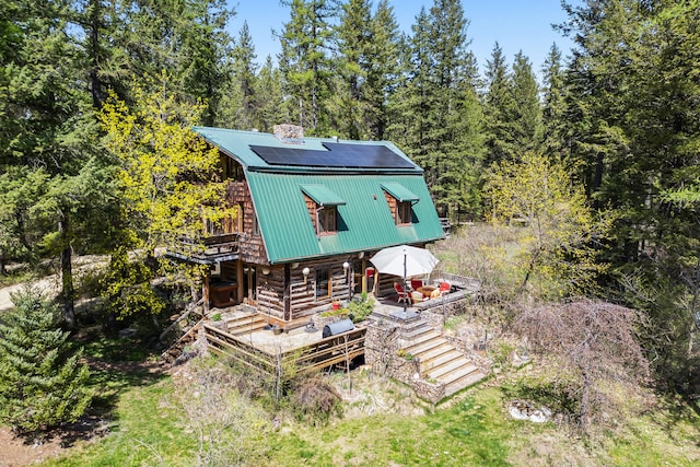 exterior space with metal roof, solar panels, a chimney, stairway, and log exterior