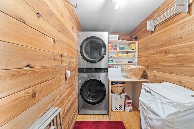 clothes washing area featuring wood walls, hardwood / wood-style flooring, laundry area, and stacked washer and dryer